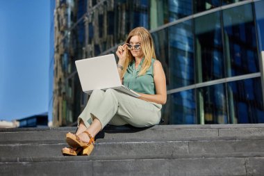 Dizüstü bilgisayarlı müdür iş merkezinin yanındaki merdivenlerde oturuyor..