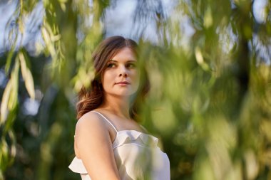 Düşünceli genç bayan yaz elbisesiyle şehir bahçesinde yürüyor..