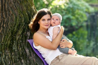 Gülümseyen kadın dışarıda yürürken küçük çocuğunu kucağına alıyor..