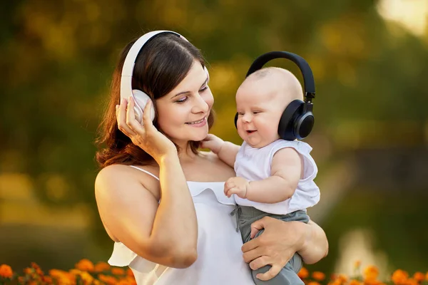 Gelukkig moeder en kind in draadloze koptelefoon tijdens het wandelen buiten. — Stockfoto