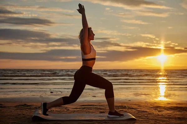 Mujer activa hace yoga durante la puesta del sol en la estera para ejercicios. — Foto de Stock