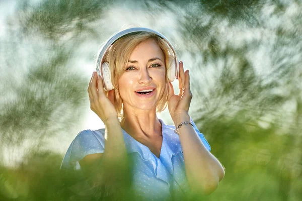 Glimlachende blonde vrouw in draadloze koptelefoon loopt in het park. — Stockfoto