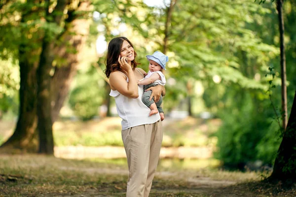 Woman talks by smartphone and holds little boy in hands. — Stock Photo, Image