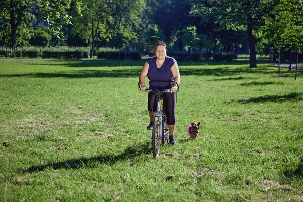 Körperlich positive Frau fährt mit Yorkshire Terrier Fahrrad im Garten. — Stockfoto