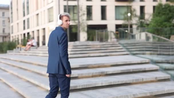Zufriedener Manager hört Musik über drahtlose Kopfhörer draußen. — Stockvideo