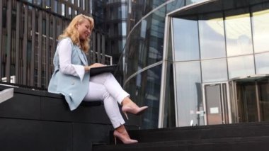 İş elbiseli kadın, ofis merkezinin yakınında otururken bilgisayarından video ile iletişim kuruyor..