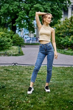 İnce bir genç kadın. 18 yaşında. Kot pantolonlu ve parkta üstten poz veriyor..