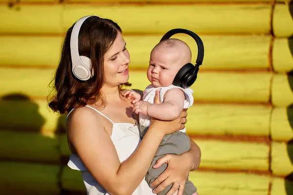 Draadloze koptelefoon op oren van moeder en baby in het openbaar park. — Stockfoto