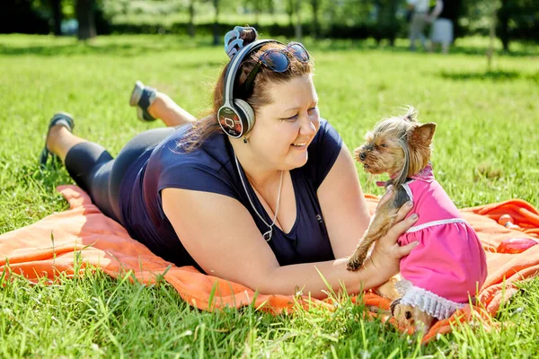 Dagadt nő fekszik a gyepen, és mosolyog Yorkshire Terrier. — Stock Fotó