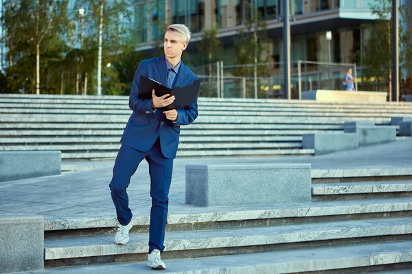 Trabajador de oficina en traje azul se destaca al aire libre con una carpeta abierta de documentos. — Foto de Stock