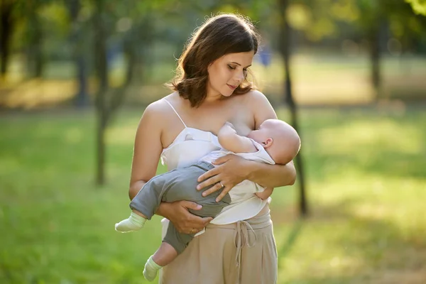 Borstvoeding in openbaar park, jonge moeder geeft haar baby borst tijdens het lopen. Stockfoto