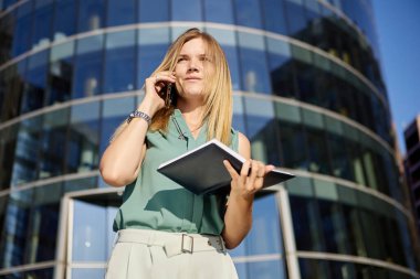 Kadın telefonla konuşuyor ve açık havada deftere bakıyor..