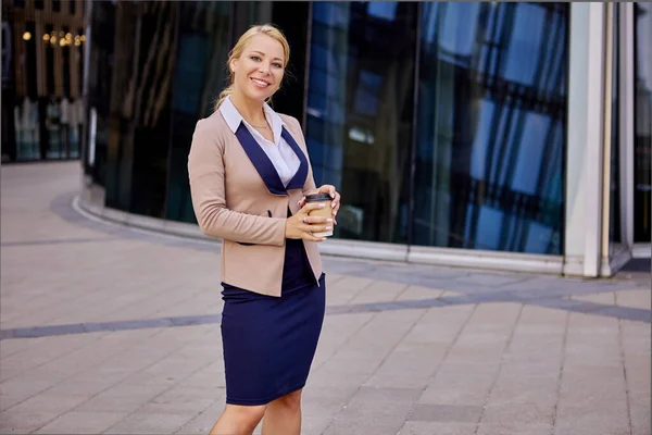 Glad kvinna i kostym står nära business center med hämtmat kaffe. — Stockfoto