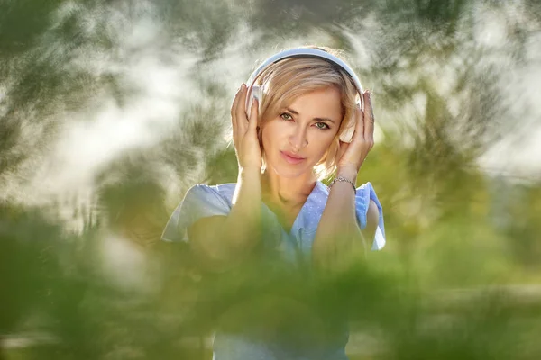 Blondynka w bezprzewodowych słuchawkach w parku publicznym. — Zdjęcie stockowe