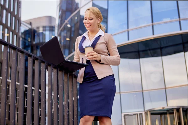 Жінка в діловому костюмі з ноутбуком і кавою біля офісної будівлі . — стокове фото