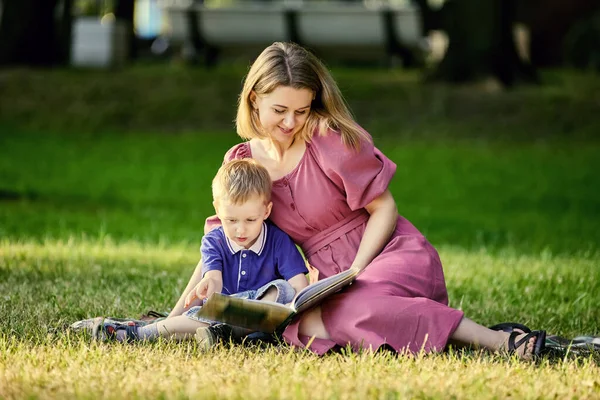 Mother and child lie on grass and read book outdoors. — Stock Photo, Image