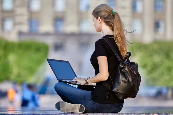 Schlanke Frau in ihren Dreißigern verrichtet Remote-Arbeit auf der Straße mit Laptop. — Stockfoto