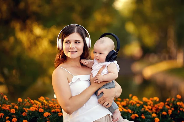 Mãe e bebê em fones de ouvido sem fio sentar no parque. — Fotografia de Stock