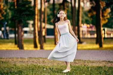 Kablosuz kulaklıklı gülümseyen zayıf kadın parkta dans ediyor..