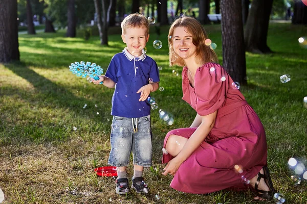 Smiling woman and boy play with bubbles outdoors. — Stock Photo, Image
