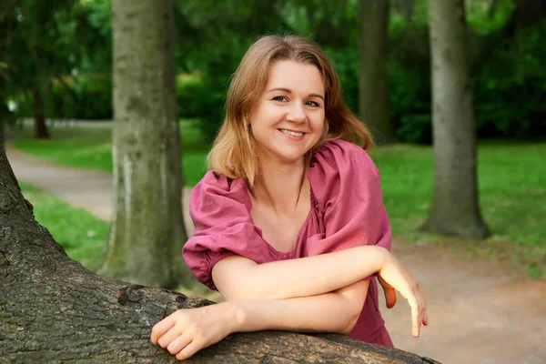 Mujer feliz se para cerca del árbol en el parque en verano. — Foto de Stock