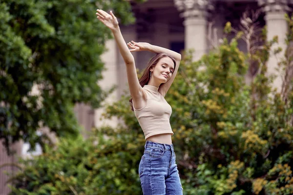 Schlanke junge Frau tanzt im Stadtgarten in der Nähe von Büschen. — Stockfoto