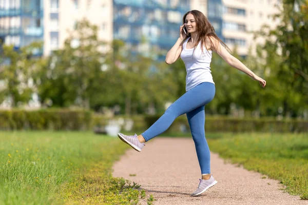 Woman talks by smartphone and makes exercises in park. — Stock Photo, Image