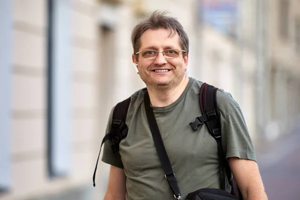 Happy middle aged man with headset and backpack outdoors. — Stock Photo, Image