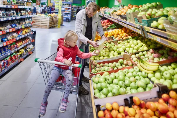 Baby i kundvagn med man väljer frukt på marknaden. — Stockfoto