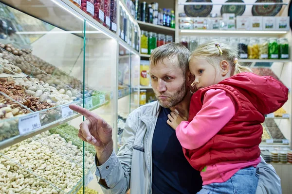 Far håller liten flicka nära monter med nötter på marknaden. — Stockfoto