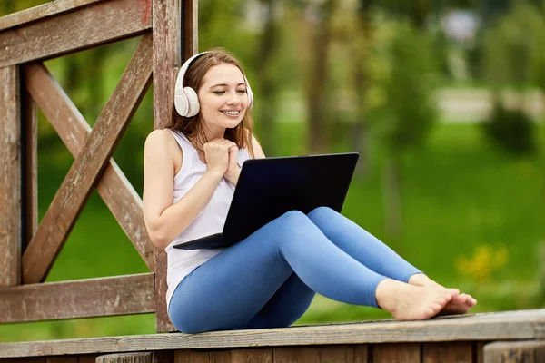 Kvinna med bärbar dator sitter utomhus i sladdlösa hörlurar. — Stockfoto