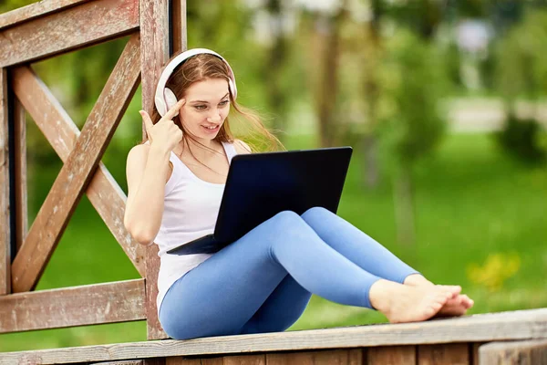 Frau mit drahtlosem Kopfhörer arbeitet mit Laptop draußen. — Stockfoto