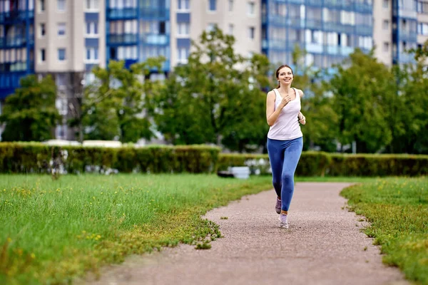 Smiling young woman is running in city garden at daytime. — Stock Photo, Image