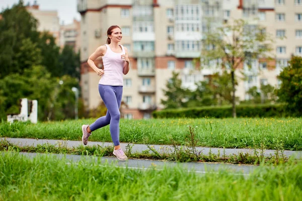 Smiling young woman in leggins runs in public park. — Stock Photo, Image