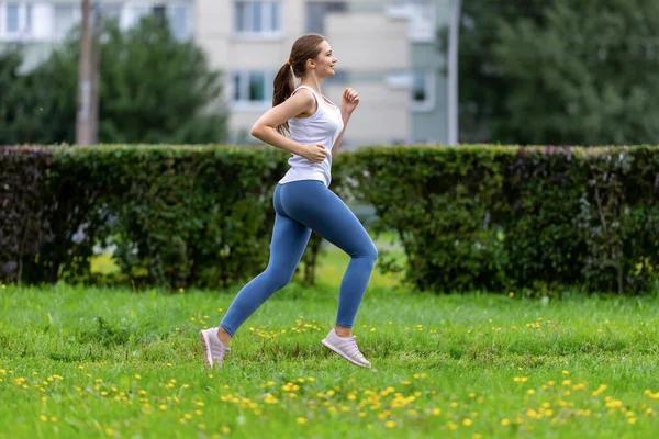 Happy woman runs on grass in city garden at daytime. — Stock Photo, Image