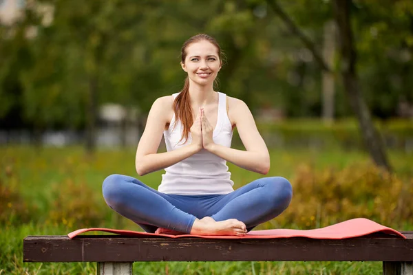 Mujer sonriente en el banco del parque hace ejercicios de yoga. — Foto de Stock