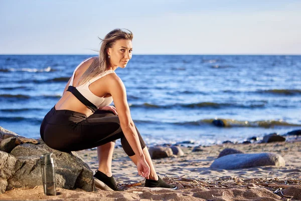 Woman is sitting near coast as rest during running. — Stock Photo, Image