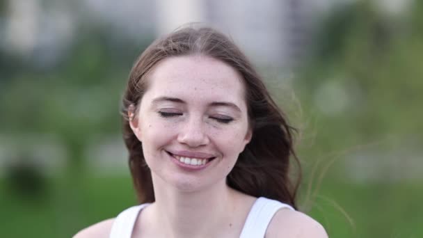 Mujer sonriente parpadea, su pelo revoloteando en el viento. — Vídeo de stock