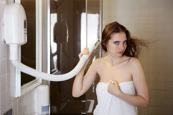 Mulher usa secador de cabelo montado na parede no banheiro do hotel. — Fotografia de Stock
