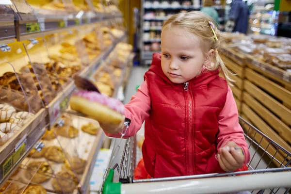 Liten flicka väljer bakverk i snabbköpet. — Stockfoto