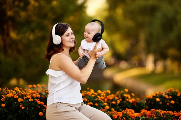 Draadloze koptelefoon voor jonge vrouw en haar baby tijdens een wandeling in de natuur op de zomeravond. — Stockfoto