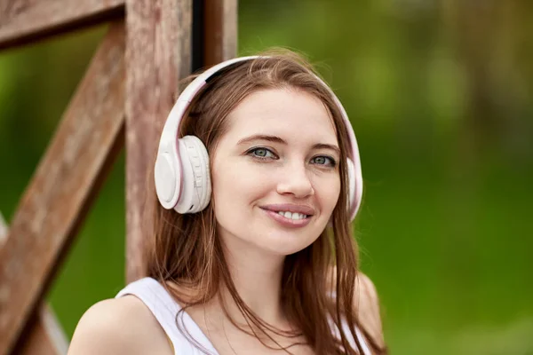 Bezprzewodowe słuchawki na miłej młodej kobiecie w parku. — Zdjęcie stockowe