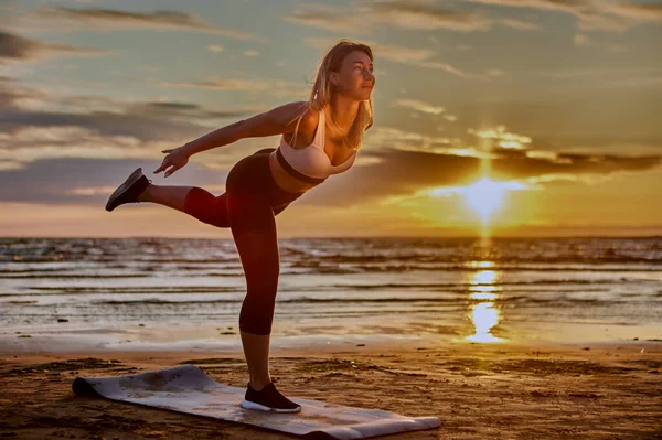 La mujer está entrenando yoga en la playa durante el atardecer. — Foto de Stock
