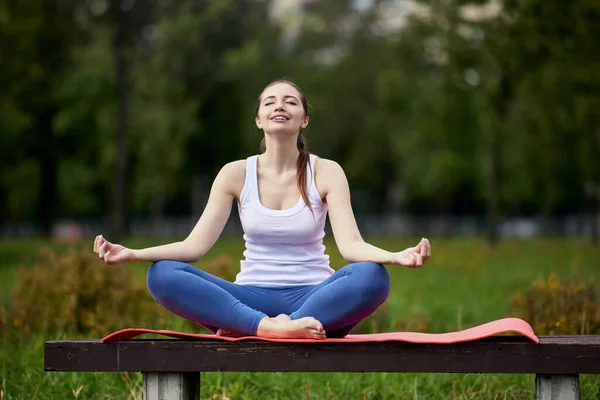 Mujer hace yoga entrenamiento mientras está sentado en el banco del parque. — Foto de Stock