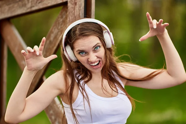 Woman in cordless headphones makes grimace outdoors. — Stock Photo, Image