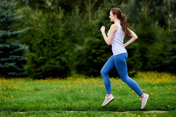 Smukła kobieta w odzieży sportowej biega w miejskim ogrodzie. — Zdjęcie stockowe