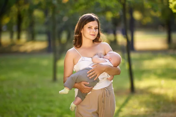 Karmienie piersią w parku publicznym przez młodą matkę na świeżym powietrzu. Obraz Stockowy