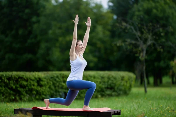Mujer sonriente haciendo ejercicio de yoga, levantando las manos mientras está de pie sobre su rodilla. — Foto de Stock