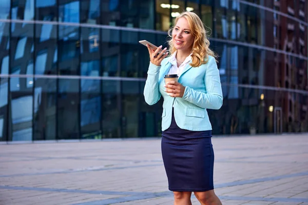 Kvinnlig kontorsarbetare med kaffe i handen talar i telefon på högtalartelefon. — Stockfoto