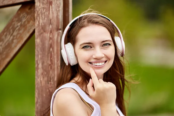 Mooie blanke vrouw is het luisteren naar muziek buiten met behulp van draadloze hoofdtelefoon. — Stockfoto